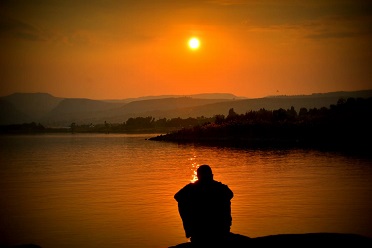 man sitting alone near water at sunset
